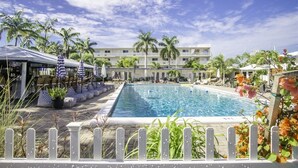 A swimming pool with lounge chairs and umbrellas, surrounded by palm trees and a hotel building. - Comfy Condo 1bed/1bath nightly condo with pool (Marathon)