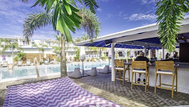 A poolside area with a hammock, striped cushions, wooden chairs, and a bar. - Comfy Condo 1bed/1bath nightly condo with pool (Marathon)
