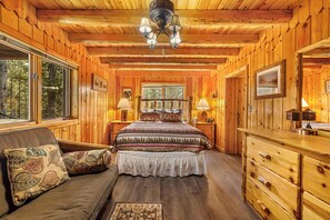 Ein Schlafzimmer in einer Blockhütte mit Bett, Schminktisch und Fenster.