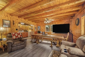 LâintĂ©rieur dâune cabane en rondins comprend une table Ă manger, des canapĂ©s, un tĂ©lĂ©viseur et un coin cuisine.