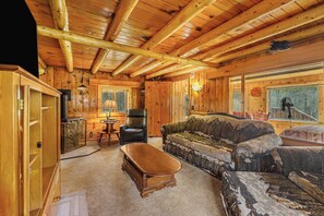 L’intérieur d’une cabane en rondins, avec un plafond en bois, un canapé, un fauteuil et une cheminée.