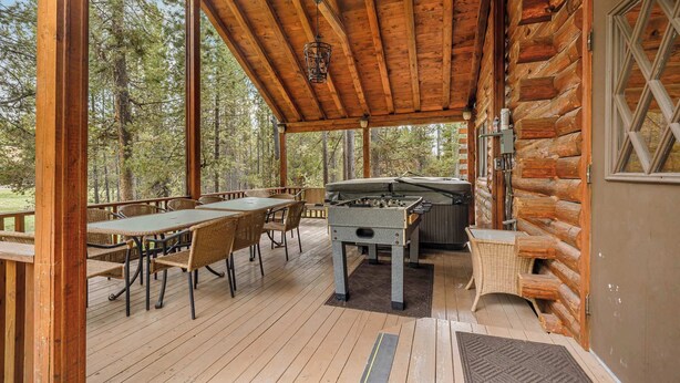 Een overdekt buitengebied met een houten tafel en stoelen, een tafelvoetbaltafel en een jacuzzi.