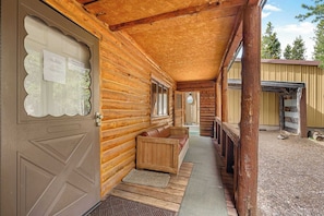 Une cabane en rondins avec un porche, des bancs en bois et une porte sur laquelle est accrochée une enseigne.
