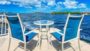A boat deck with two blue chairs and a round table, overlooking a calm sea with distant islands. - Palm Point 3bed/2bath single family home with open water views, private pool & dockage (Marathon)