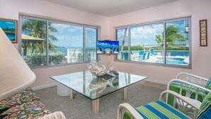 A room with a glass table, a ceiling fan, and a view of a pool and palm trees. - Palm Point 3bed/2bath single family home with open water views, private pool & dockage (Marathon)