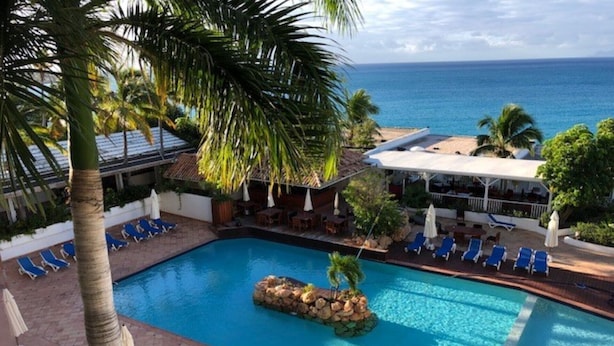 A pool area with a view of the ocean, lounge chairs, and palm trees.