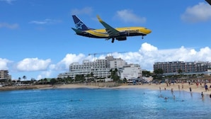 An airplane flying over a beach with buildings in the background.