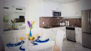 A modern kitchen with white cabinets, a microwave, a refrigerator, and a dining area with a table set for two.