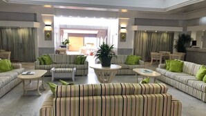 A spacious lobby with striped sofas and armchairs, a central coffee table, and a large window providing natural light.
