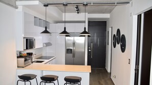 A modern kitchen with stainless steel appliances, a central island with stools, pendant lighting, and a dark door in the background. - Cozy Stays Cayala Apartments 2 (Zone 16)