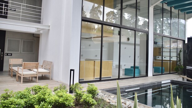 A modern building with large glass windows, a pool, and outdoor seating with chairs. - Cozy Stays Cayala Apartments 2 (Zone 16)