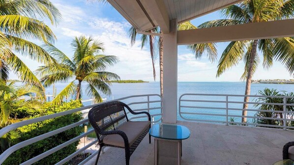 A balcony with a chair and table, overlooking a body of water with palm trees.