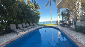 A swimming pool with lounge chairs, a view of the ocean, and a building with a balcony.