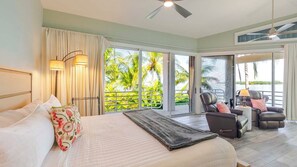 Une chambre d’hôtel équipée d’un lit, d’une chaise, d’une table, d’un ventilateur de plafond et de grandes portes-fenêtres coulissantes donnant sur un balcon avec vue sur les palmiers.