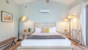 Een slaapkamer met een bed, nachtkastjes, een vloerlamp, een airconditioner en een raam met gordijnen.