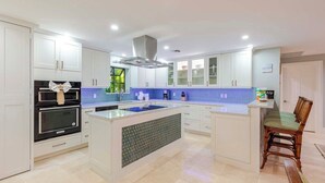 A modern kitchen with white cabinets, a central island, and a built-in oven. - Shangri-La 3 Bedroom 3 Baths Gulf Front Estate (Marathon)