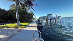 Un muelle frente al agua con un bote, palmeras y un camino pavimentado.