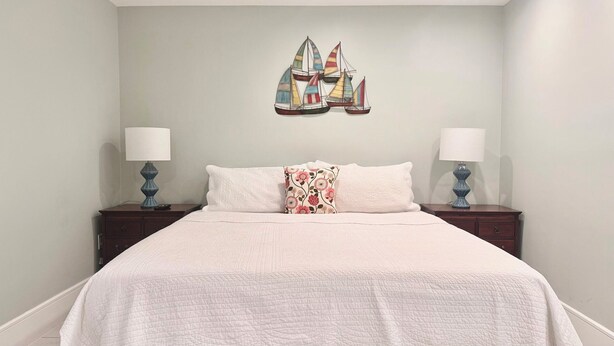Een slaapkamer met een bed, twee nachtkastjes, twee lampen en een decoratie aan de muur.