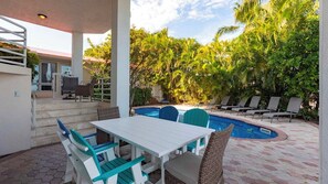 A covered outdoor area with a pool, lounge chairs, and a table with chairs.