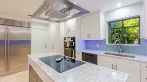 A modern kitchen with a built-in stove, stainless steel appliances, and a window with a view of greenery.