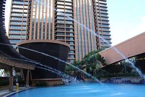 A modern hotel with a large pool, a covered area with a curved roof, and a tall building in the background. - Times Square Service Suite By DaisyHomes (Kuala Lumpur)