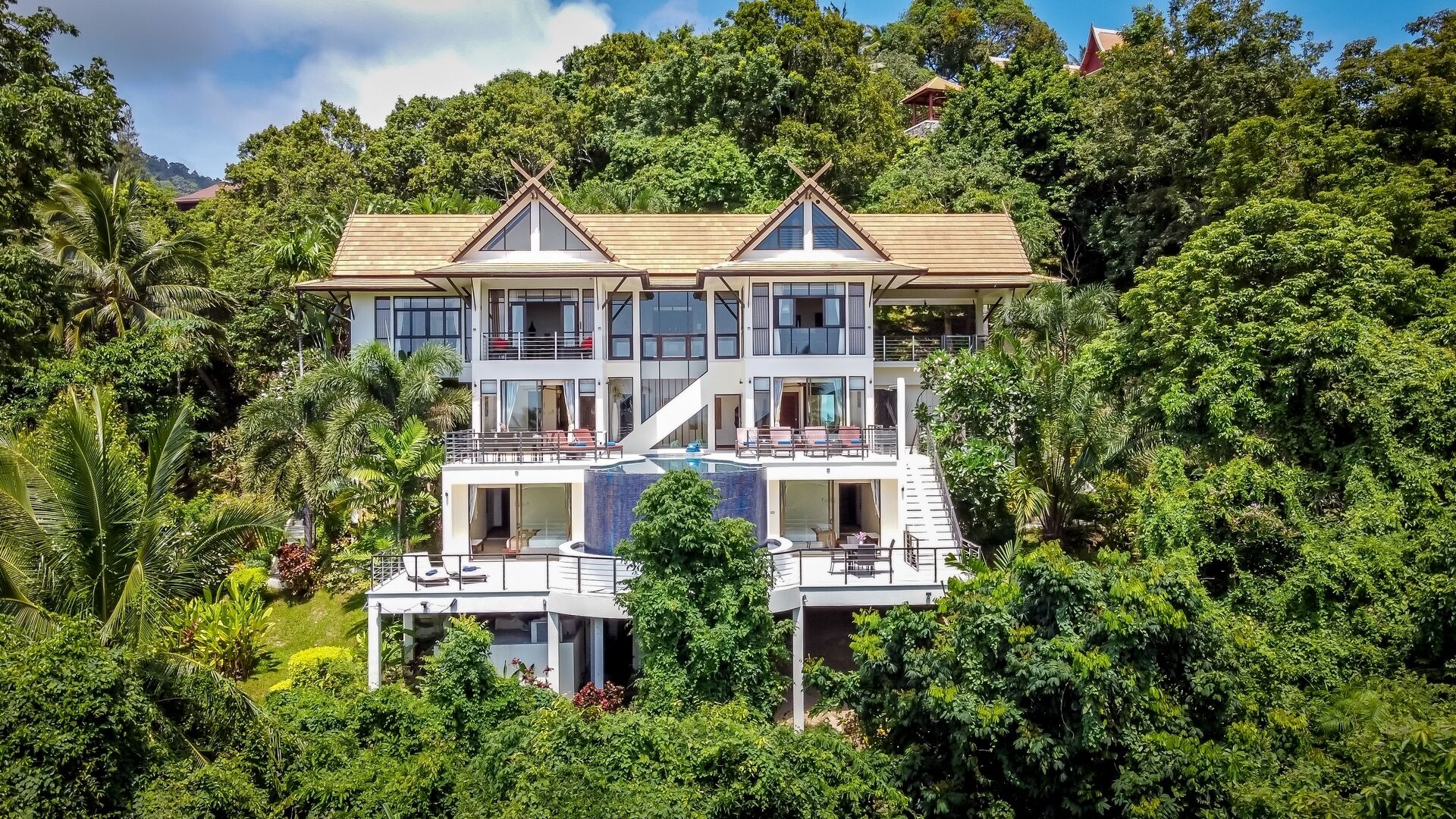 A multi-story house with a large balcony, surrounded by lush greenery.