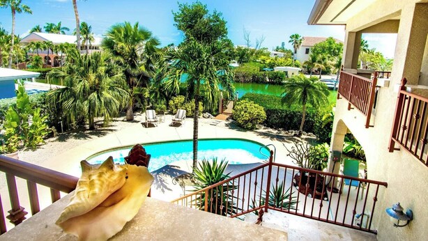 A poolside view with a clear blue pool, palm trees, and a balcony with a railing. - Beachy Keen House 3/2 Water View Pool Home with Dock (Marathon)
