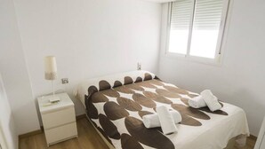 Un lit bien fait, recouvert d’une couvre-lit à motifs, une table de chevet avec une lampe et une fenêtre avec des stores.