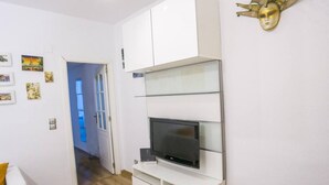 Un salon moderne avec un téléviseur à écran plat, des meubles blancs et un masque décoratif accroché au mur.