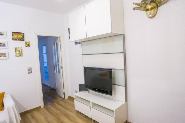 A modern living room with a flat-screen TV, white cabinets, and a decorative mask on the wall.