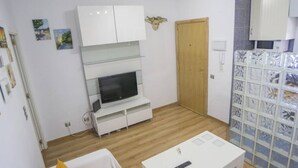 Un espace de vie compact avec un téléviseur posé sur un meuble blanc, une porte en bois et un mur recouvert de carreaux, agrémenté de boîtes de rangement.