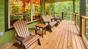 A covered outdoor seating area with wooden chairs and tables, large windows, and a wooden deck. - Splashin' Around! 3 Bedroom with a Pool! Minutes from downtown Pigeon Forge. (Sevierville)