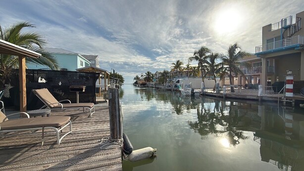 A waterfront resort with a wooden dock, lounge chairs, and a calm water body reflecting the sky. - Blue Marlin 2/2 Pool home with 35` Dock Easy Access to Atlantic (Marathon)
