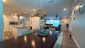 A modern kitchen with white cabinets, a dining table with chairs, a ceiling fan, and a living area with a sofa and a coffee table. - Blue Marlin 2/2 Pool home with 35` Dock Easy Access to Atlantic (Marathon)