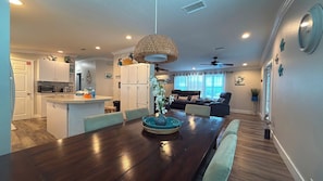 A modern kitchen with white cabinets, a dining table with chairs, a ceiling fan, and a living area with a sofa and a coffee table.