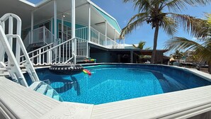A swimming pool with a white deck, a lifeguard stand, and a house with a blue exterior in the background. - Blue Marlin 2/2 Pool home with 35` Dock Easy Access to Atlantic (Marathon)