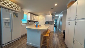 A modern kitchen with a central island, bar stools, and a refrigerator with a water dispenser. - Blue Marlin 2/2 Pool home with 35` Dock Easy Access to Atlantic (Marathon)
