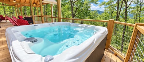 A hot tub on a wooden deck with a view of trees and mountains.