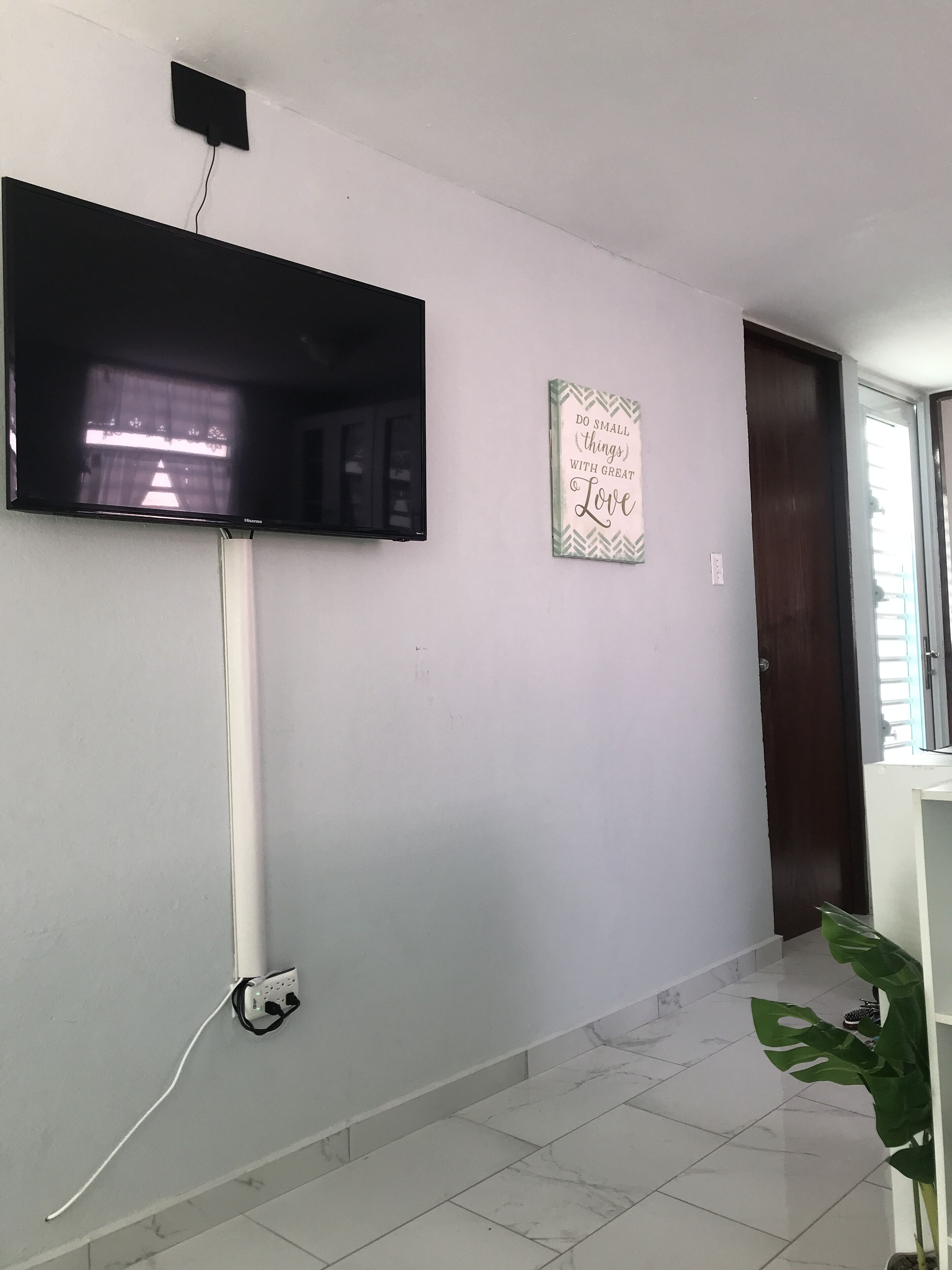 A hallway with a flat-screen TV mounted on the wall, a power outlet, and a motivational quote sign.