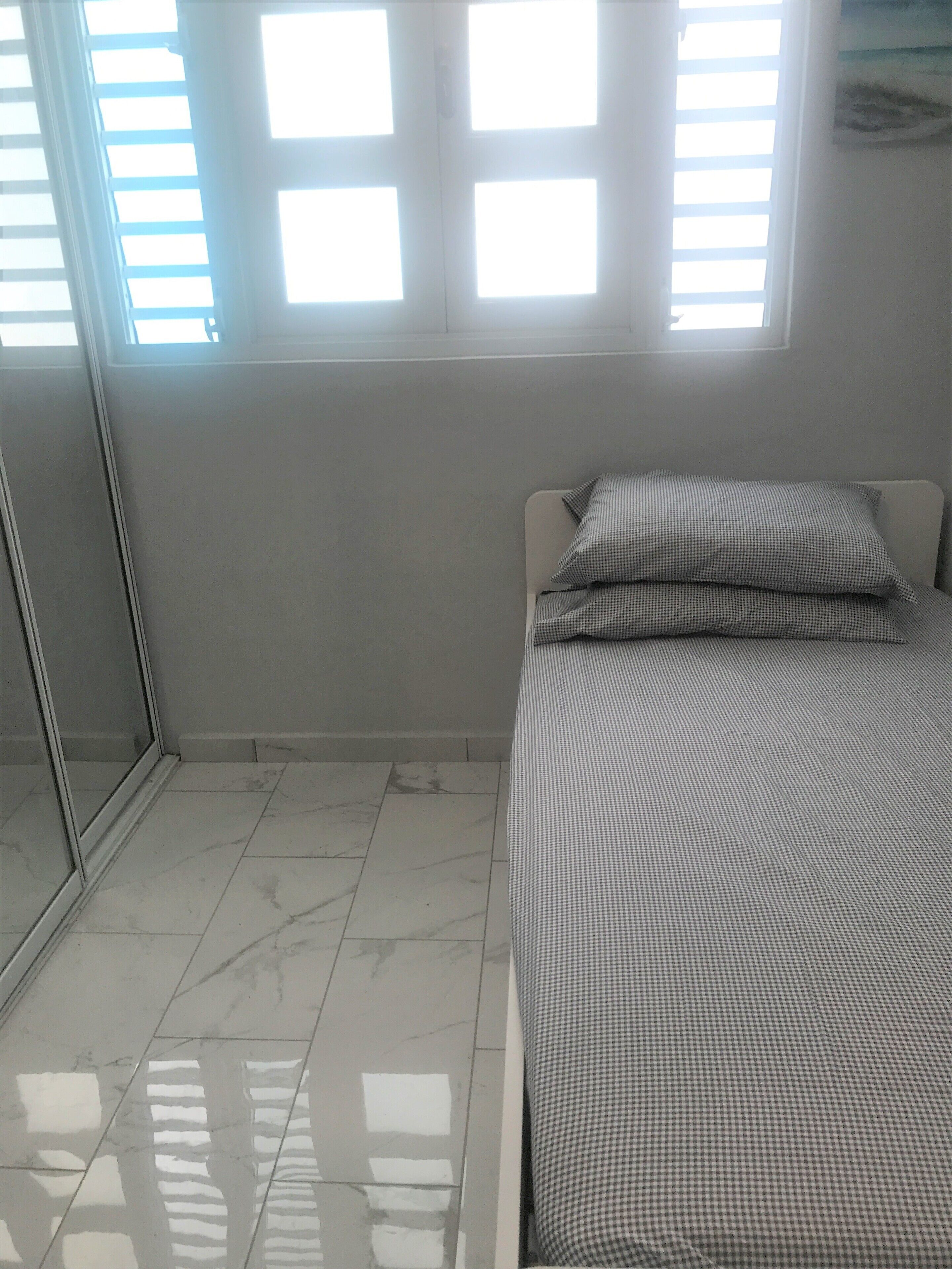 A bedroom with a bed, checkered bedding, a window with blinds, and a tiled floor.