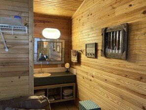 A wooden cabin interior with a mirror, a hanging towel, a framed sign, and a small shelf.
