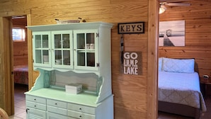 A wooden cabin interior with a bed, a cabinet with glass doors, and two signs on the wall reading "KEYS" and "GO JUMP INTO THE LAKE". - Wolf Pack place of Pomme de Terre Lake! (Pittsburg)