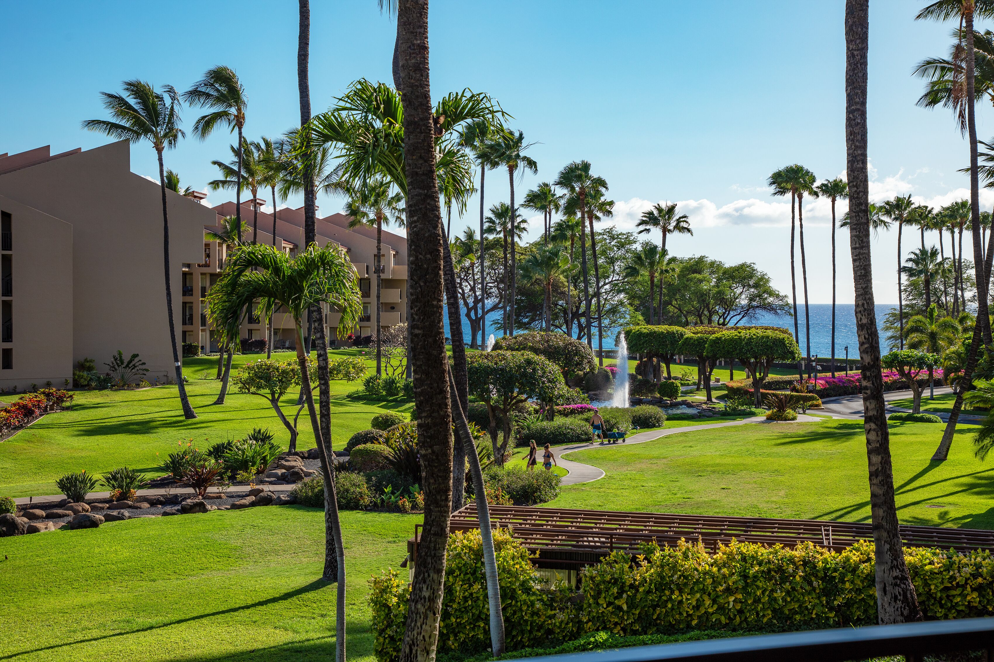 A resort with a well-maintained lawn, palm trees, and a view of the ocean.