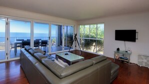 Amplia sala de estar con un gran ventanal corredizo que da a un patio exterior, un sofá cómodo, una mesita y un televisor montado.