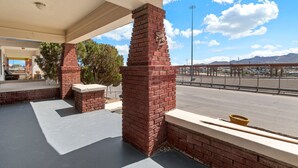 A covered outdoor area with brick pillars, a concrete floor, and a view of a parking lot and mountains in the background.