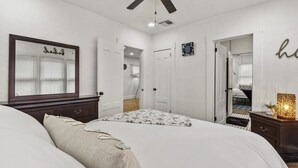 A bedroom with a large bed, a ceiling fan, a mirror, and a dresser with a lamp.