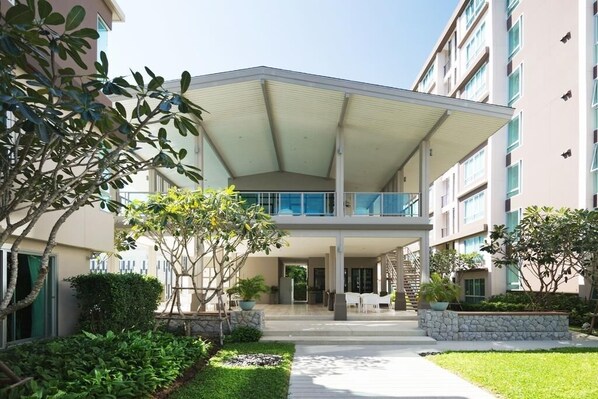 Un hotel moderno con un área exterior cubierta, una piscina y un jardín cuidado.