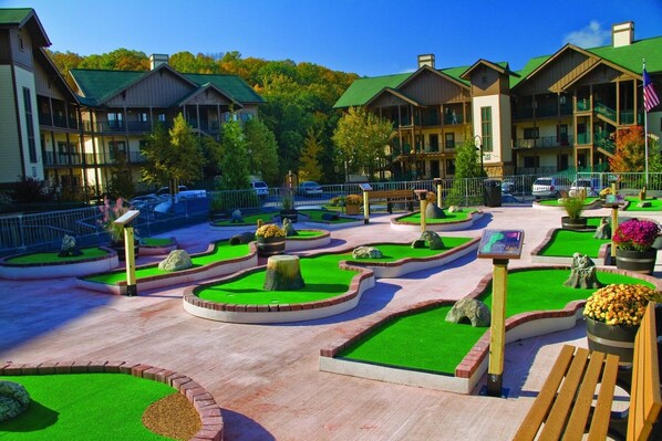 A resort with multiple-story buildings, a landscaped courtyard with green lawns and pathways, and a parking area with cars.