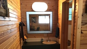 Ein kleines, gemütliches Badezimmer mit Holzwänden, einem Waschbecken, einem Spiegel und einem Fenster.