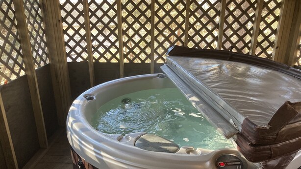 Ein Whirlpool mit Holzterrasse und einem Gitterzaun im Hintergrund.